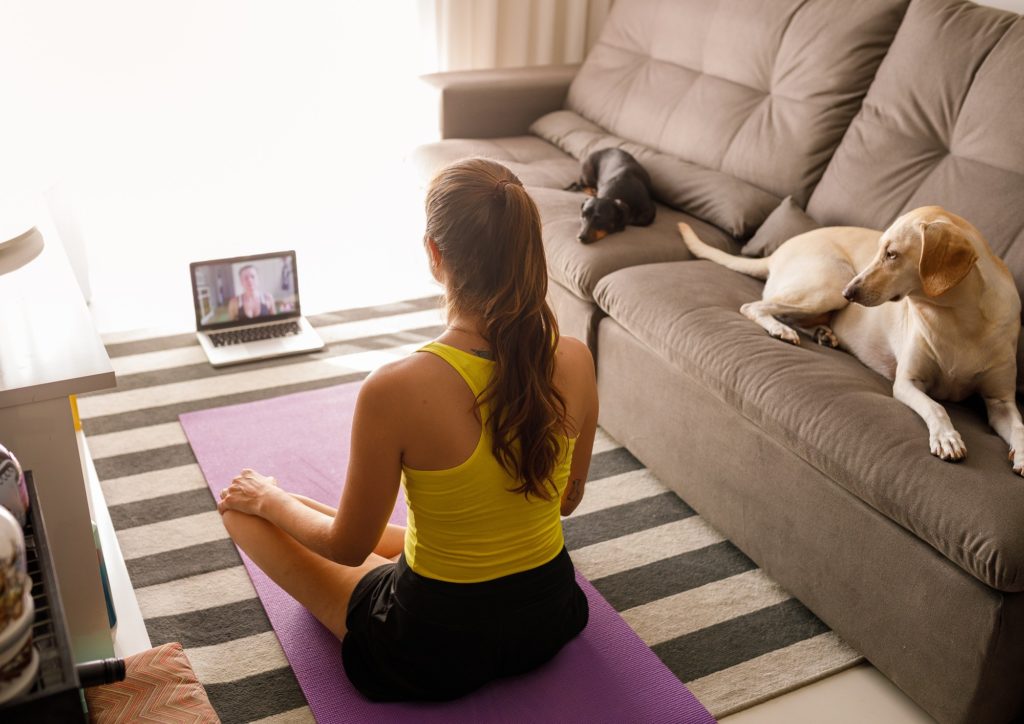 Fitness woman at home practicing yoga with trainer using video call