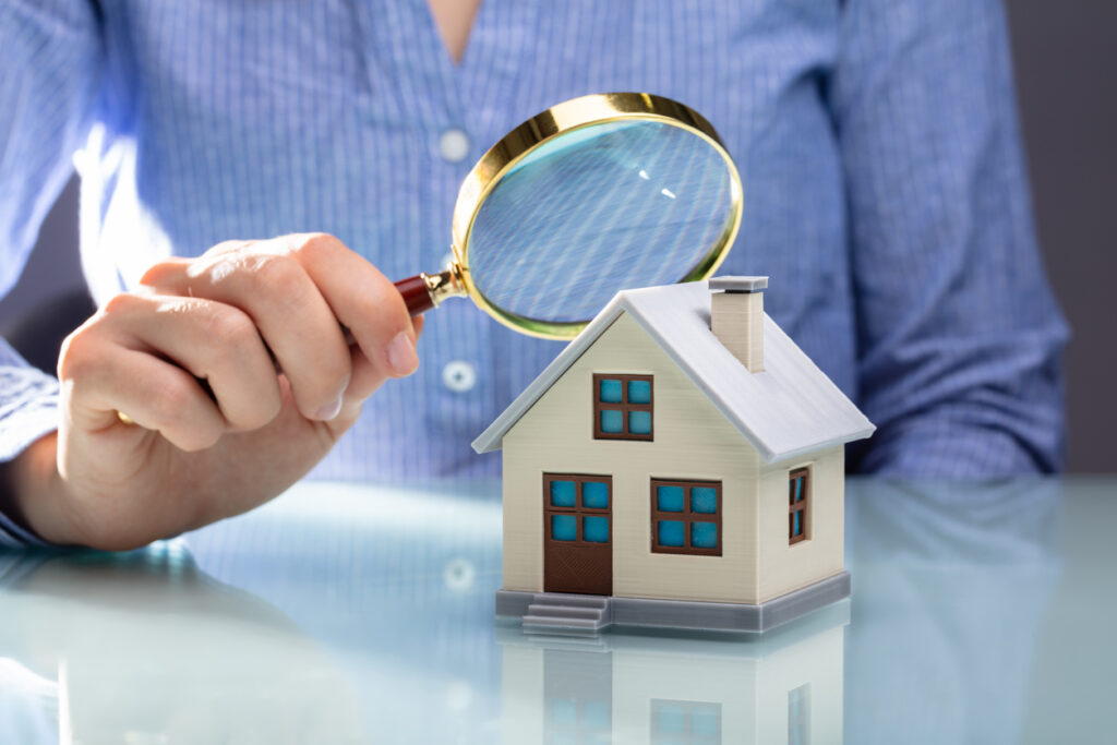 man holding magnifying glass above mini house