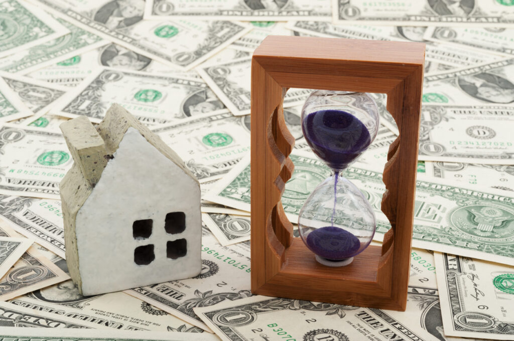 hourglass and house above dollars