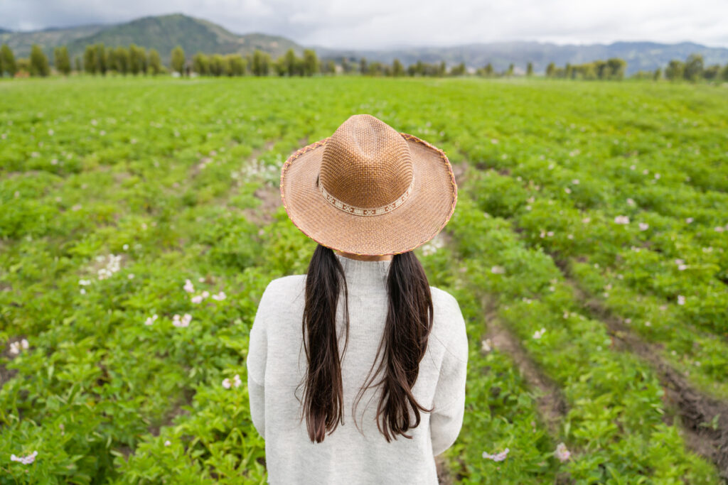 Latin American girl at a farm looking at the potato crop while wearing a hat agriculture